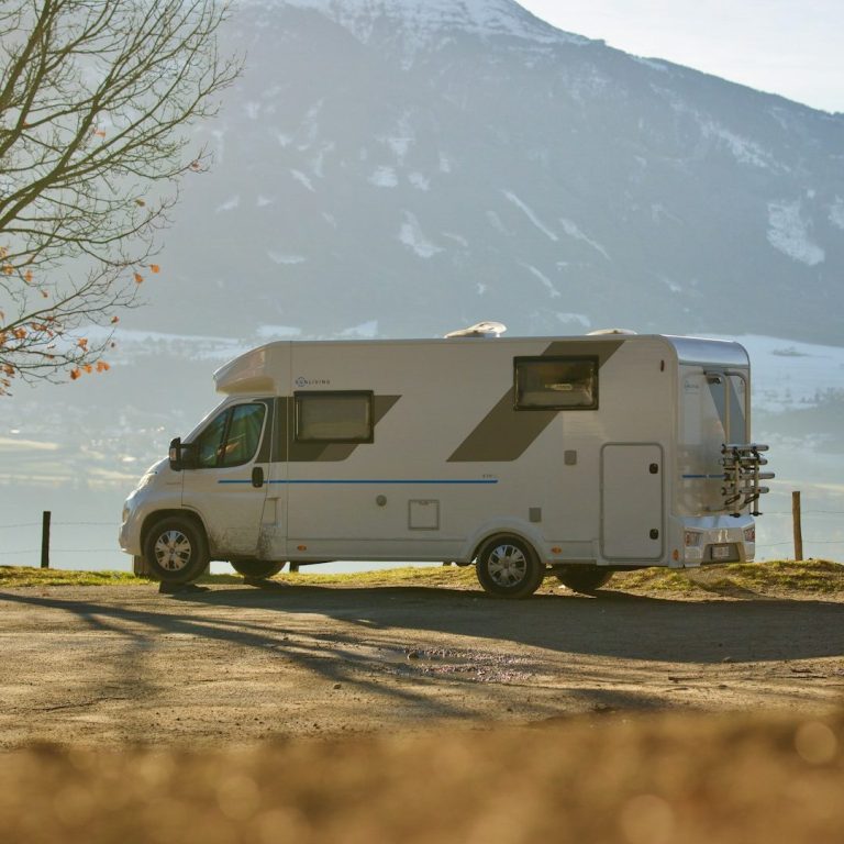 Wohnmobil steht an einem See mit Bergen und Bäumen im Hintergrund.