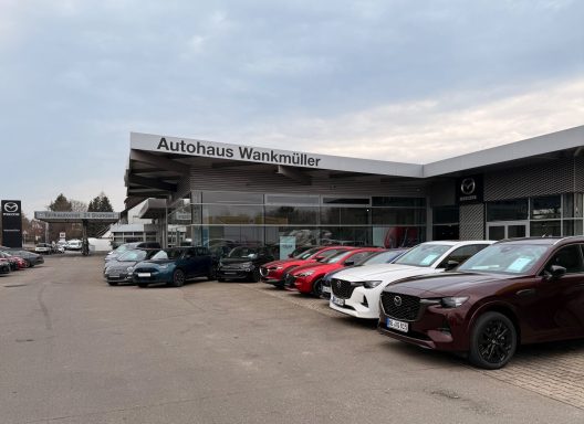 Autohaus mit verschiedenen Mazda und Fiat Fahrzeugen auf dem Parkplatz, unter bewölktem Himmel.