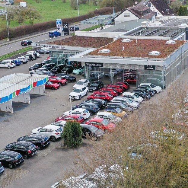 Autohändler mit vielen Fahrzeugen auf dem Parkplatz und einem modernen Gebäude.