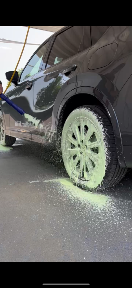 Schwarzes Auto mit grünem Felgenreiniger auf den Rädern besprüht wird.