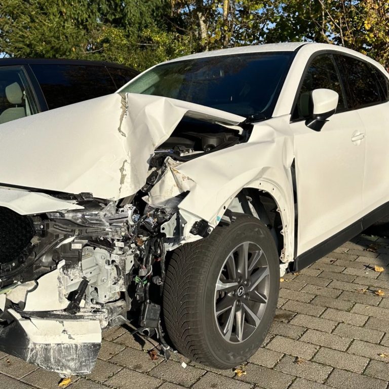 Weißer SUV mit frontalem Unfallschaden auf einem gepflasterten Parkplatz.