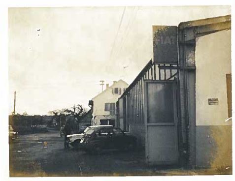 Ein alter Parkplatz mit Autos und einer alten Werkstatt im Hintergrund.